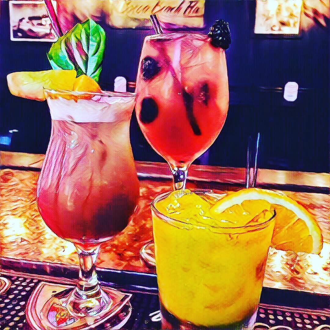 Three garnished craft cocktails lined up on a lit bar top