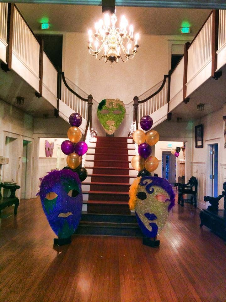 Mardi Gras themed event entry with masks and balloon columns beneath a chandelier